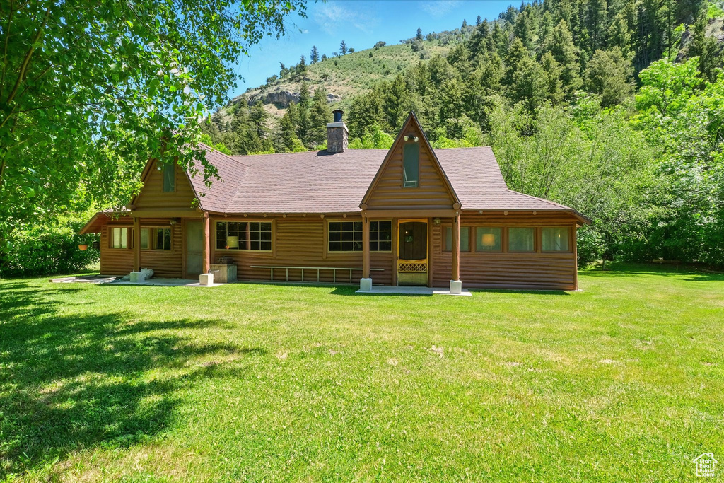 View of front of property featuring a front yard, faux log siding, a chimney, and roof with shingles