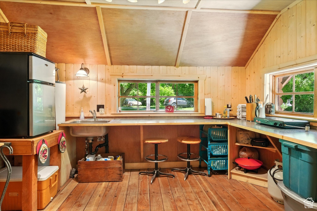 Bar with freestanding refrigerator, lofted ceiling, hardwood / wood-style floors, and wooden walls