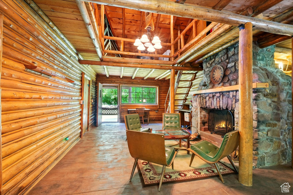 Sitting room with a chandelier, log walls, hardwood / wood-style floors, and a stone fireplace