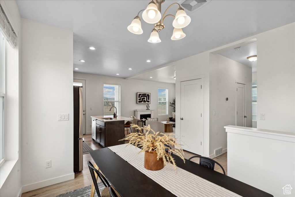 Dining space with a chandelier, light wood-type flooring, recessed lighting, and a fireplace