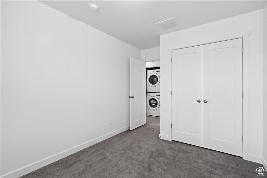 Unfurnished bedroom with stacked washer / drying machine, dark colored carpet, and a closet