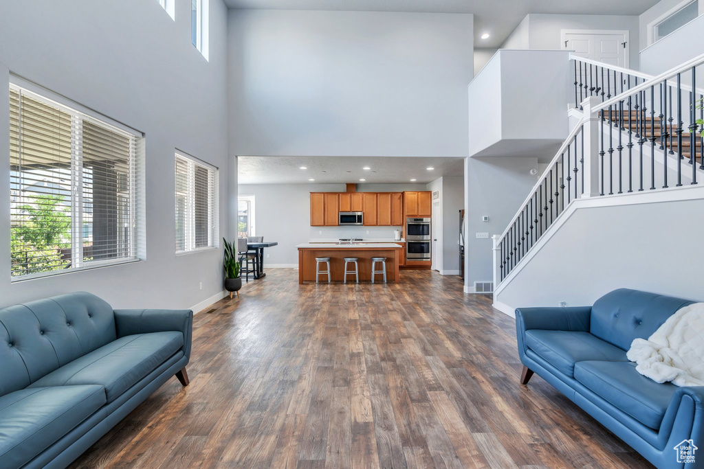 Living area featuring a high ceiling, stairs, dark wood finished floors, and healthy amount of natural light