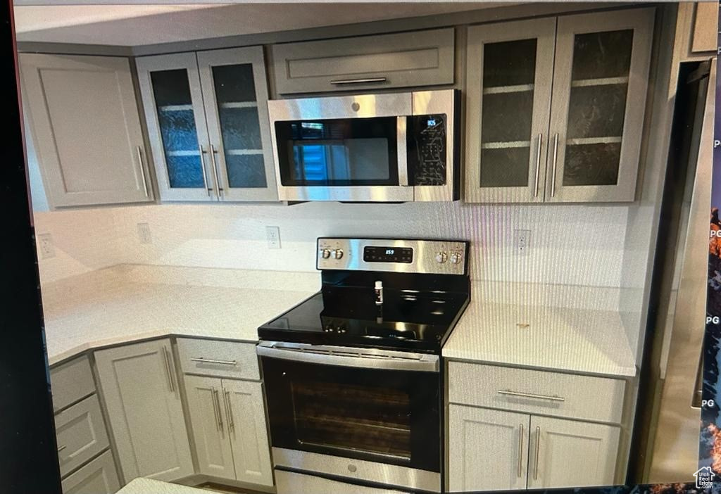 Kitchen featuring stainless steel appliances, light countertops, glass insert cabinets, and gray cabinets