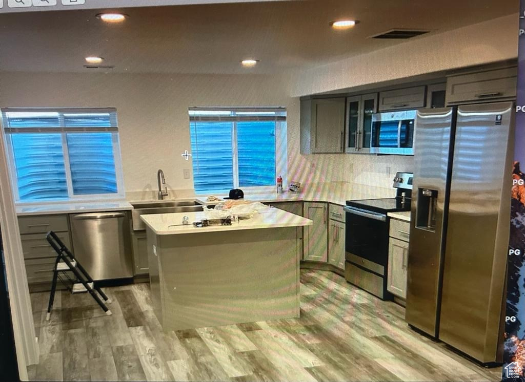 Kitchen featuring appliances with stainless steel finishes, light countertops, light wood-style floors, glass insert cabinets, and recessed lighting