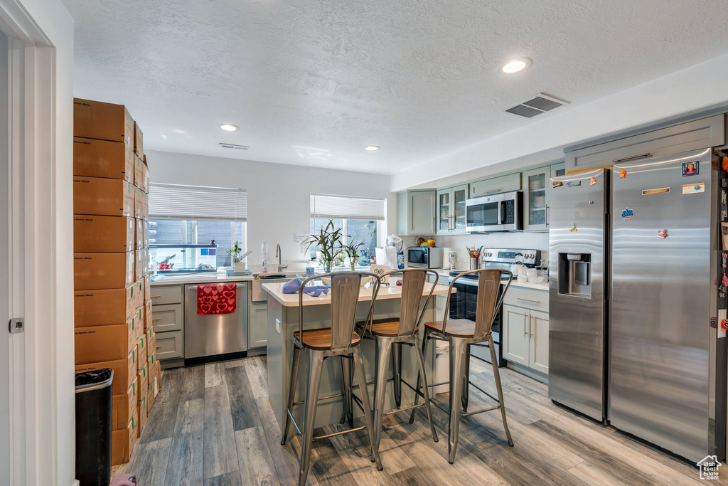 Kitchen featuring stainless steel appliances, light countertops, wood finished floors, glass insert cabinets, and a breakfast bar area