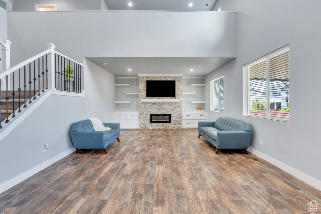 Living room featuring wood finished floors, a fireplace, a high ceiling, stairs, and recessed lighting