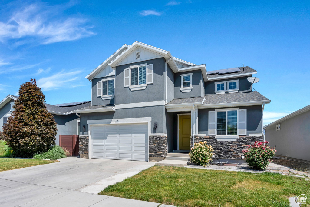 View of front of house with stucco siding, solar panels, stone siding, and concrete driveway