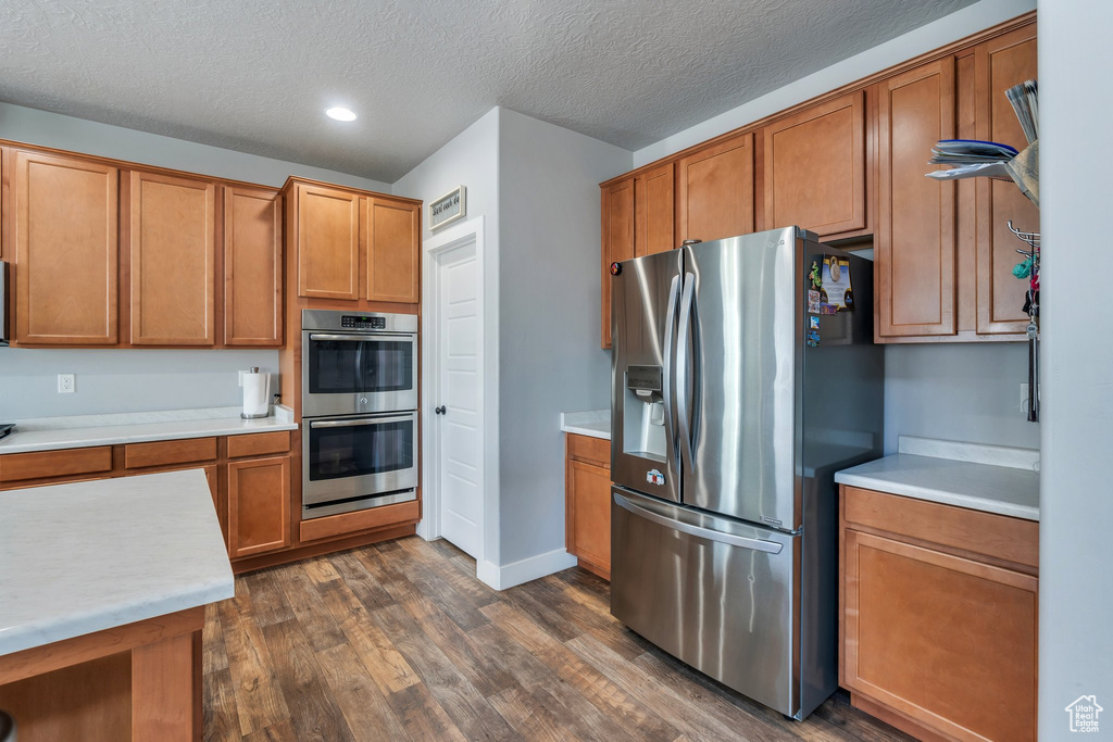Kitchen featuring stainless steel appliances, dark wood-style floors, brown cabinetry, light countertops, and recessed lighting