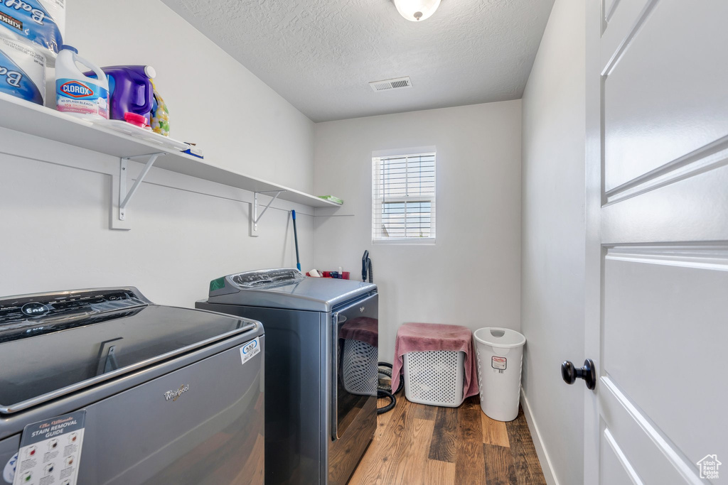 Washroom with wood finished floors, washer and dryer, and a textured ceiling