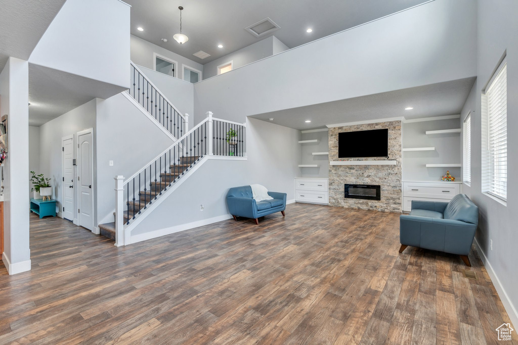 Living room featuring wood finished floors, stairs, a towering ceiling, a stone fireplace, and recessed lighting