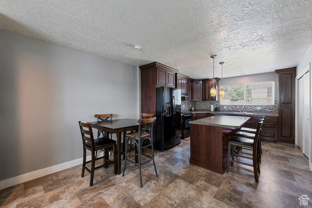 Kitchen with black appliances, dark brown cabinets, dark countertops, a kitchen island, and a textured ceiling