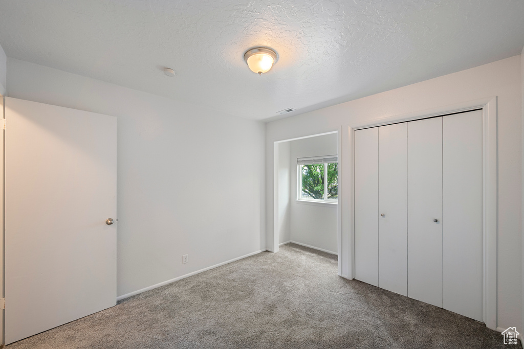 Unfurnished bedroom featuring carpet, a textured ceiling, and a closet