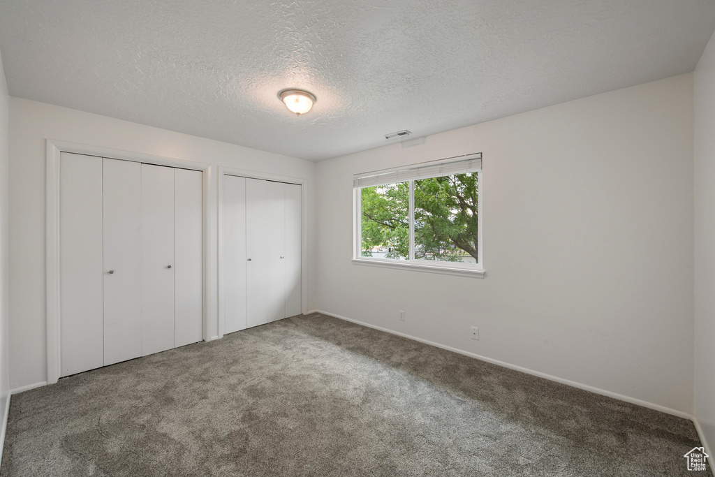 Unfurnished bedroom with multiple closets, carpet flooring, a textured ceiling, and baseboards