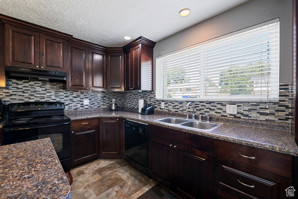 Kitchen with under cabinet range hood, black appliances, dark countertops, a sink, and decorative backsplash
