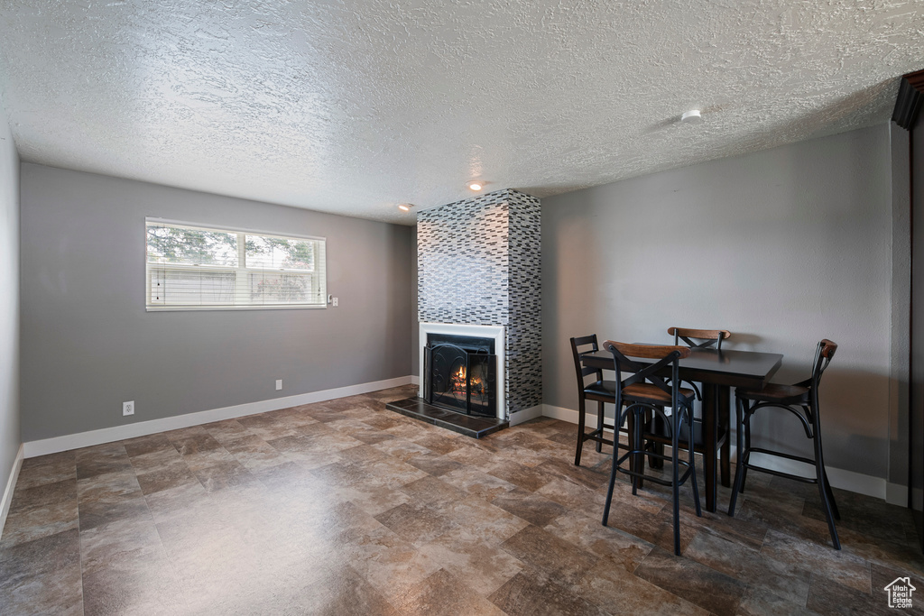 Dining space with a tiled fireplace, a textured ceiling, baseboards, and stone finish flooring