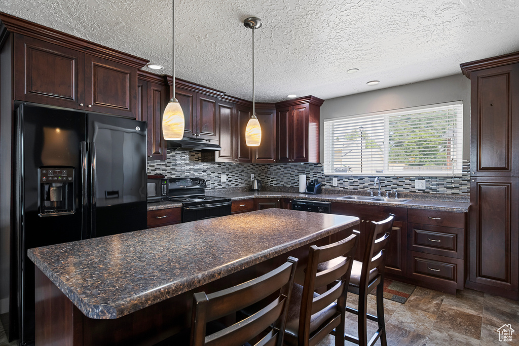 Kitchen featuring black appliances, a sink, dark countertops, under cabinet range hood, and a textured ceiling