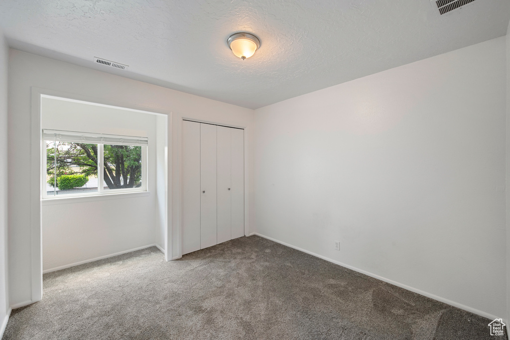 Unfurnished bedroom featuring carpet floors, a textured ceiling, baseboards, and a closet