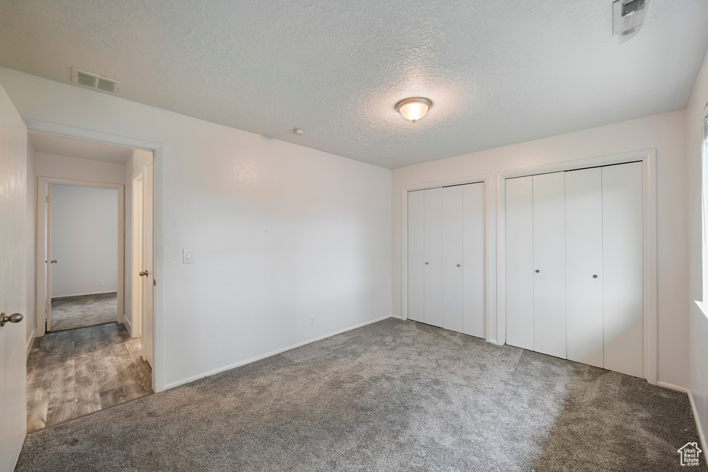 Unfurnished bedroom with multiple closets, carpet, a textured ceiling, and baseboards