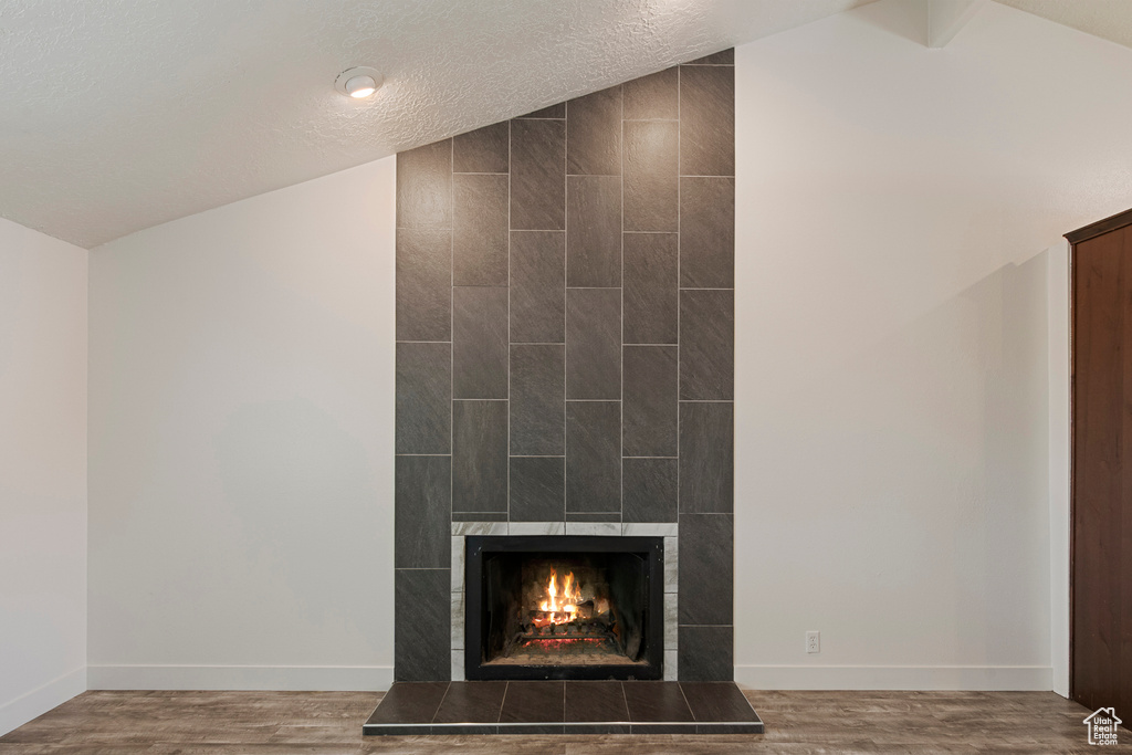 Detailed view of a tiled fireplace, baseboards, wood finished floors, and a textured ceiling