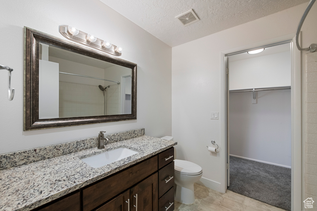 Full bath featuring vanity, toilet, a walk in closet, a textured ceiling, and a shower