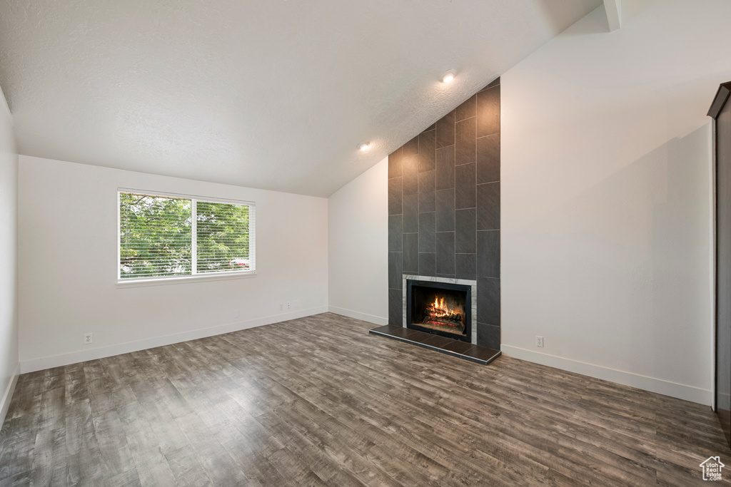 Unfurnished living room featuring vaulted ceiling, dark wood-style floors, a tiled fireplace, and baseboards