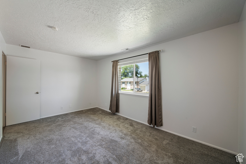 Carpeted spare room with a textured ceiling and baseboards