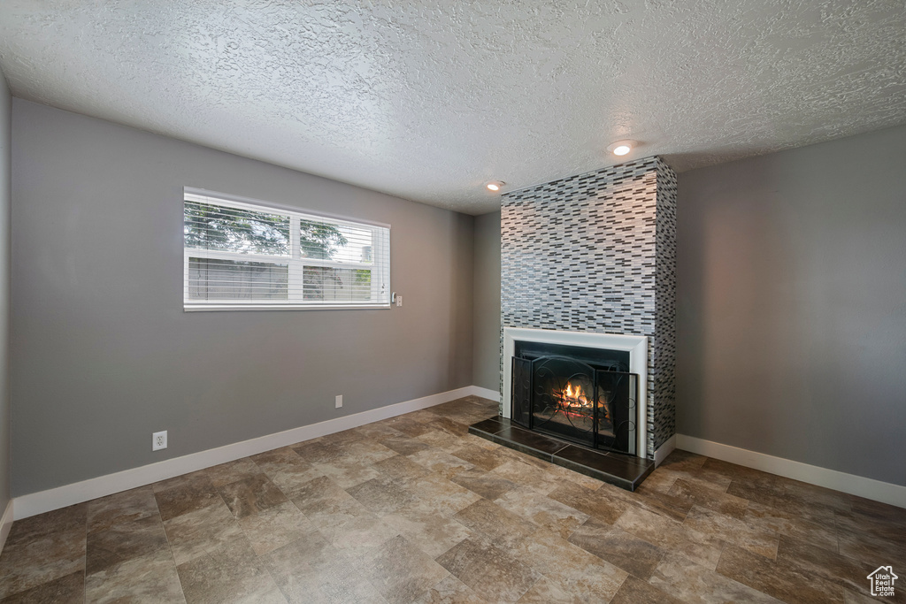 Unfurnished living room with a warm lit fireplace, a textured ceiling, baseboards, stone finish floors, and recessed lighting
