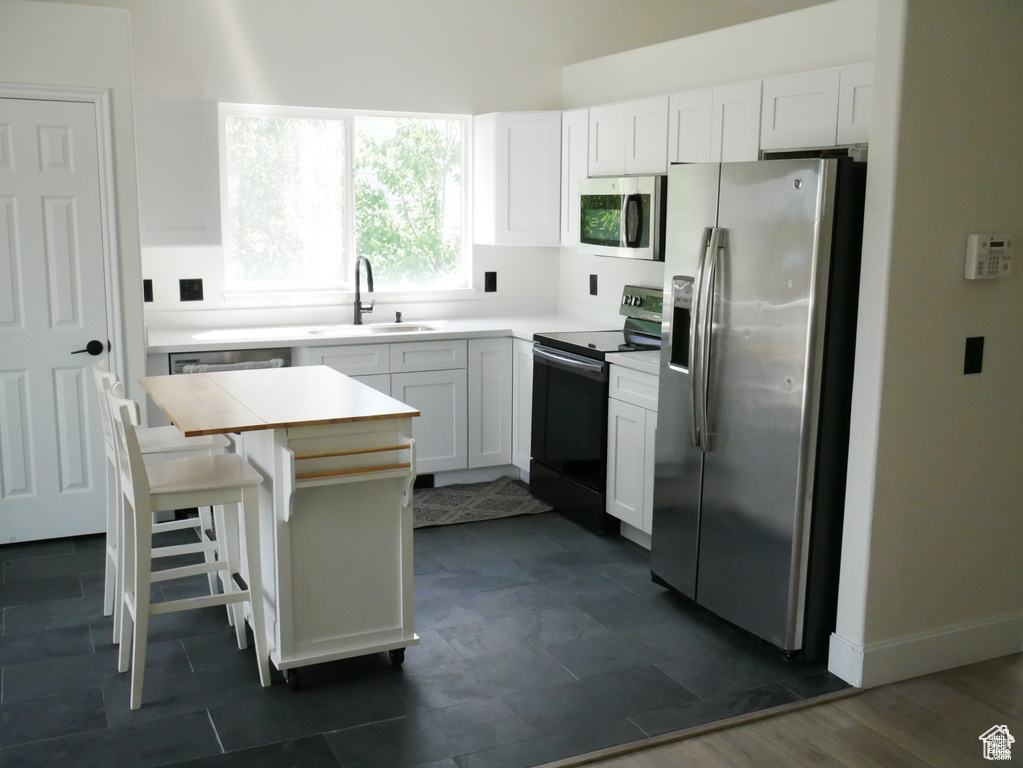 Kitchen with stainless steel appliances, white cabinets, a breakfast bar, and light countertops