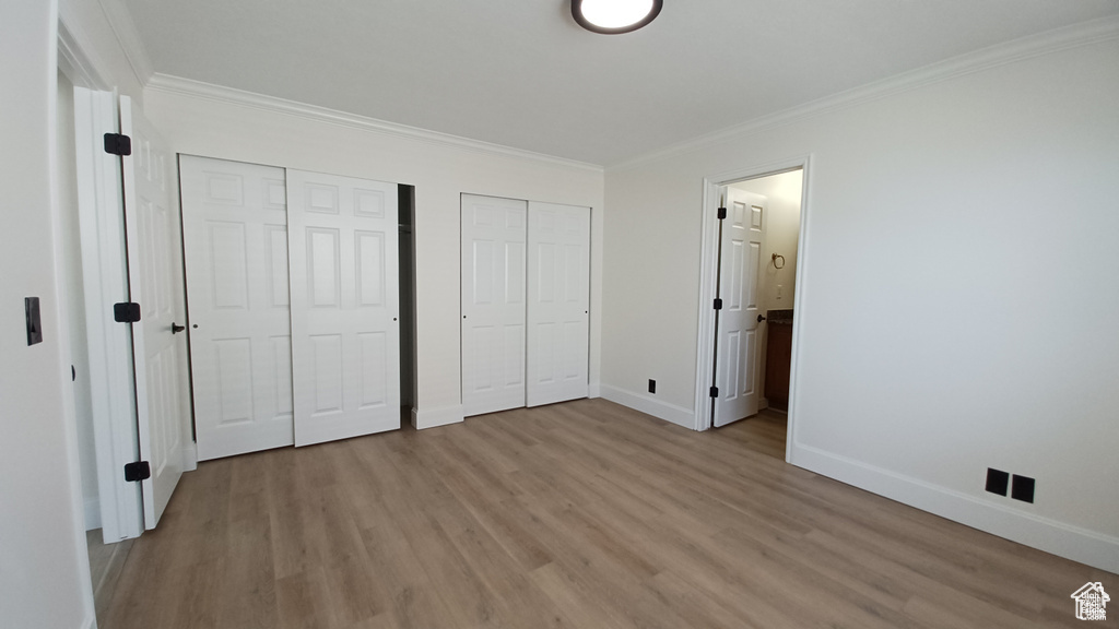 Unfurnished bedroom featuring multiple closets, light wood-type flooring, crown molding, and ensuite bath
