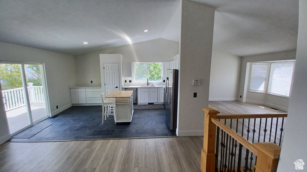 Kitchen featuring lofted ceiling, white cabinetry, a center island, appliances with stainless steel finishes, and a kitchen bar