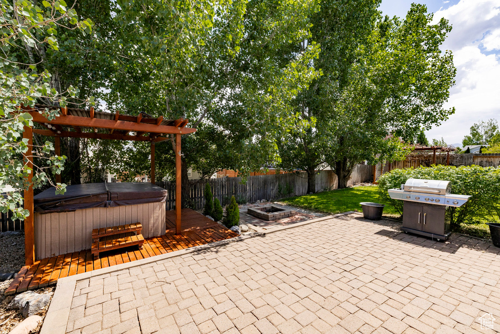 Fenced backyard with a hot tub, a patio, grilling area, a fire pit, and a wooden deck