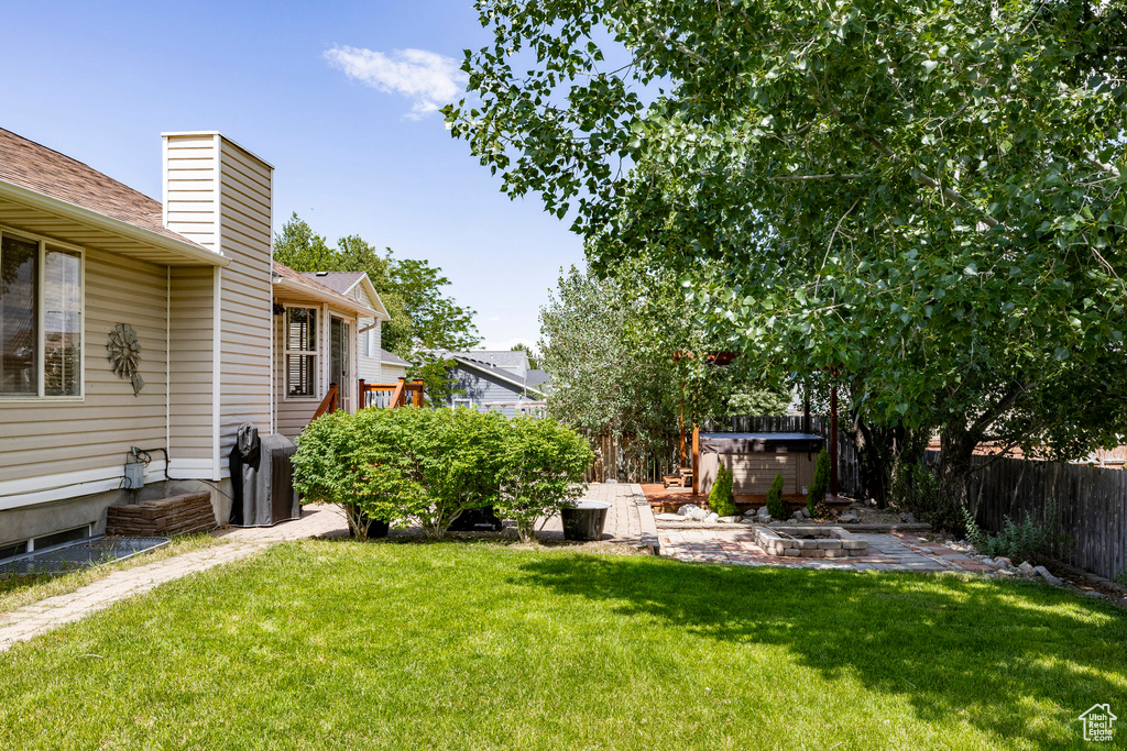 Fenced backyard with a covered hot tub, a patio, and an outdoor fire pit