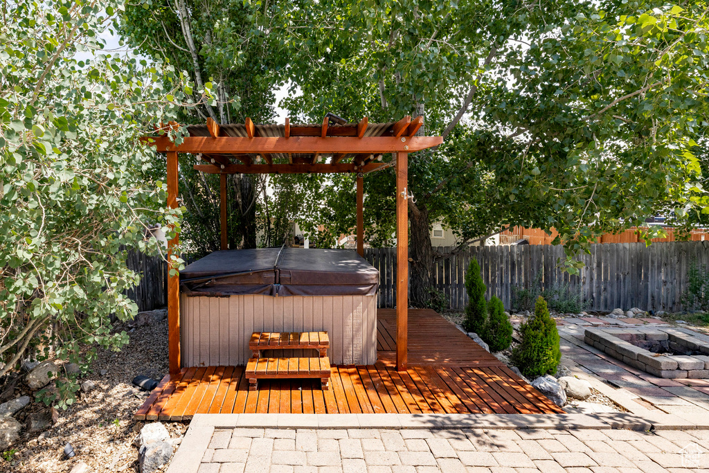 Wooden deck with a hot tub, an outdoor fire pit, a fenced backyard, and a pergola