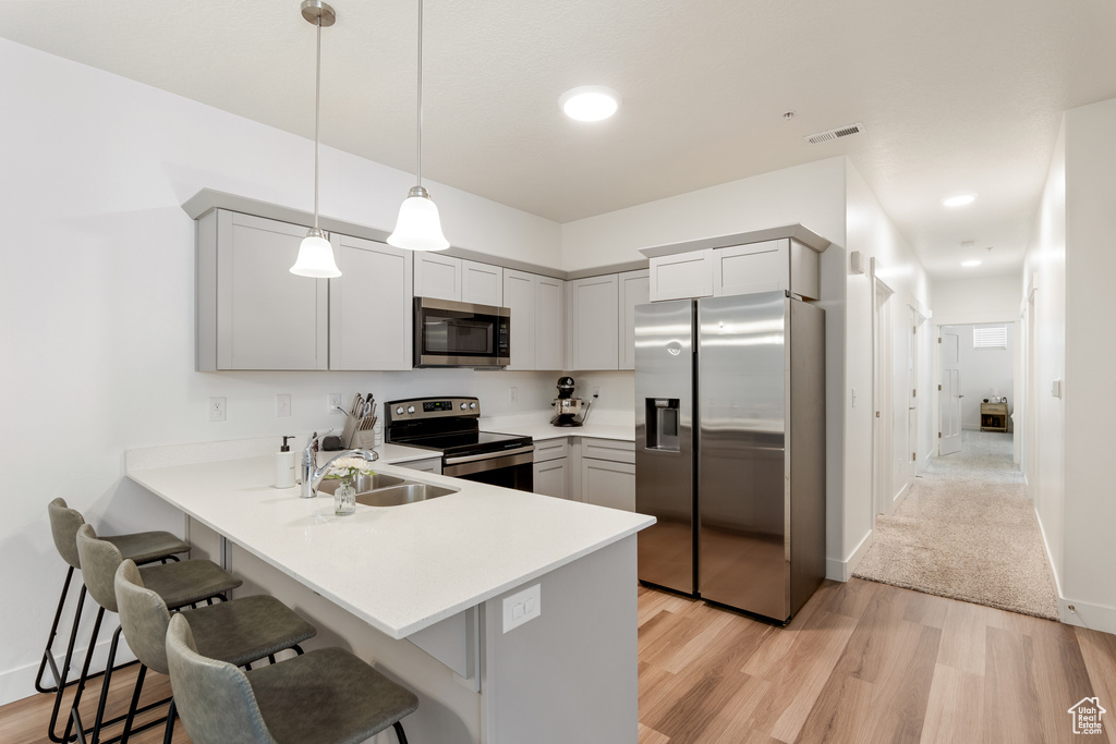 Kitchen featuring stainless steel appliances, a kitchen bar, a peninsula, light wood-style flooring, and light countertops