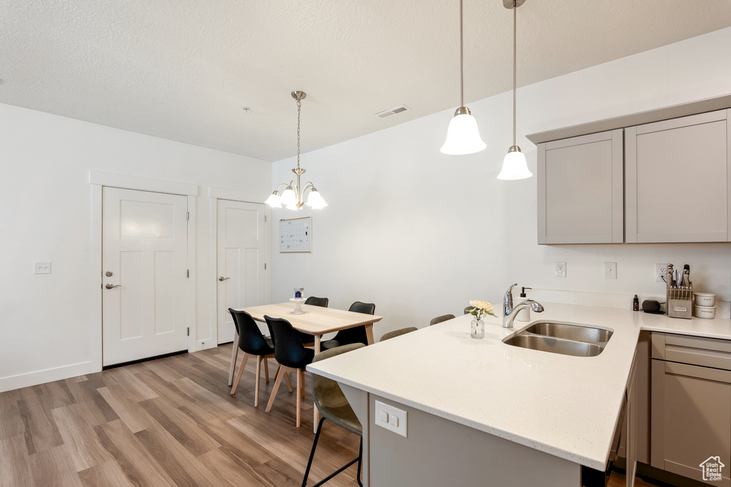 Kitchen with gray cabinets, light countertops, light wood-type flooring, a peninsula, and hanging light fixtures