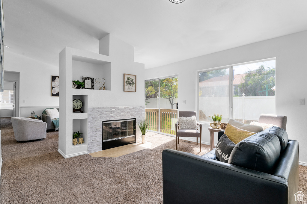 Living room with carpet flooring, a stone fireplace, and vaulted ceiling