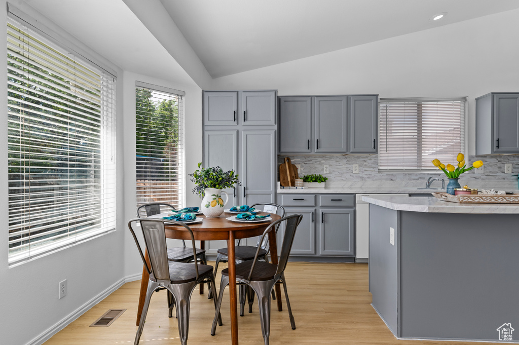 Kitchen featuring gray cabinetry, lofted ceiling, light countertops, tasteful backsplash, and light wood-style flooring