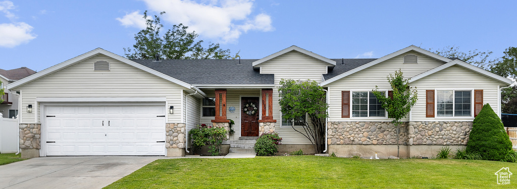 View of front facade with stone siding, concrete driveway, a garage, and a front lawn