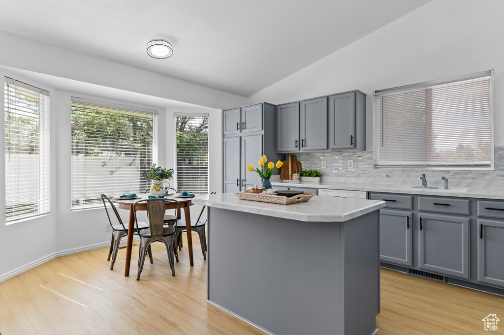 Kitchen featuring gray cabinets, backsplash, light wood finished floors, a kitchen island, and lofted ceiling