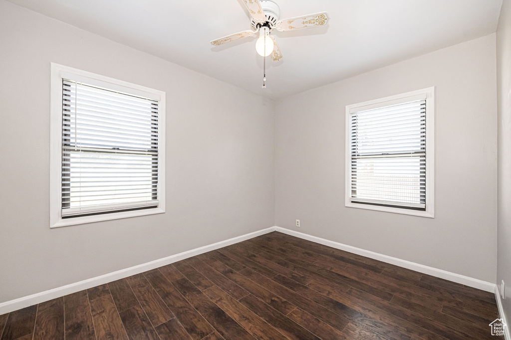 Spare room with healthy amount of natural light, baseboards, dark wood-type flooring, and a ceiling fan