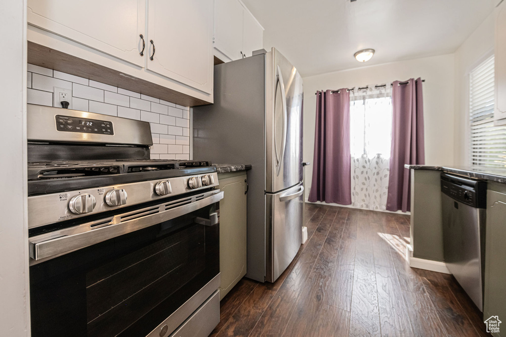 Kitchen with stainless steel appliances, dark wood-style flooring, backsplash, and white cabinetry