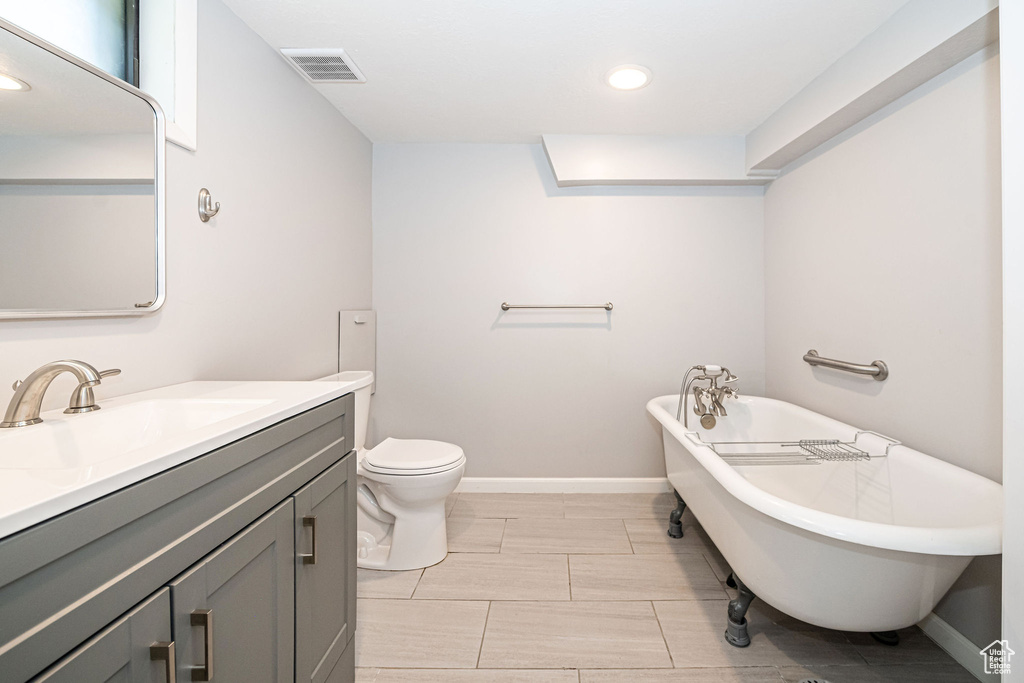 Full bathroom featuring a freestanding bath, vanity, toilet, baseboards, and recessed lighting