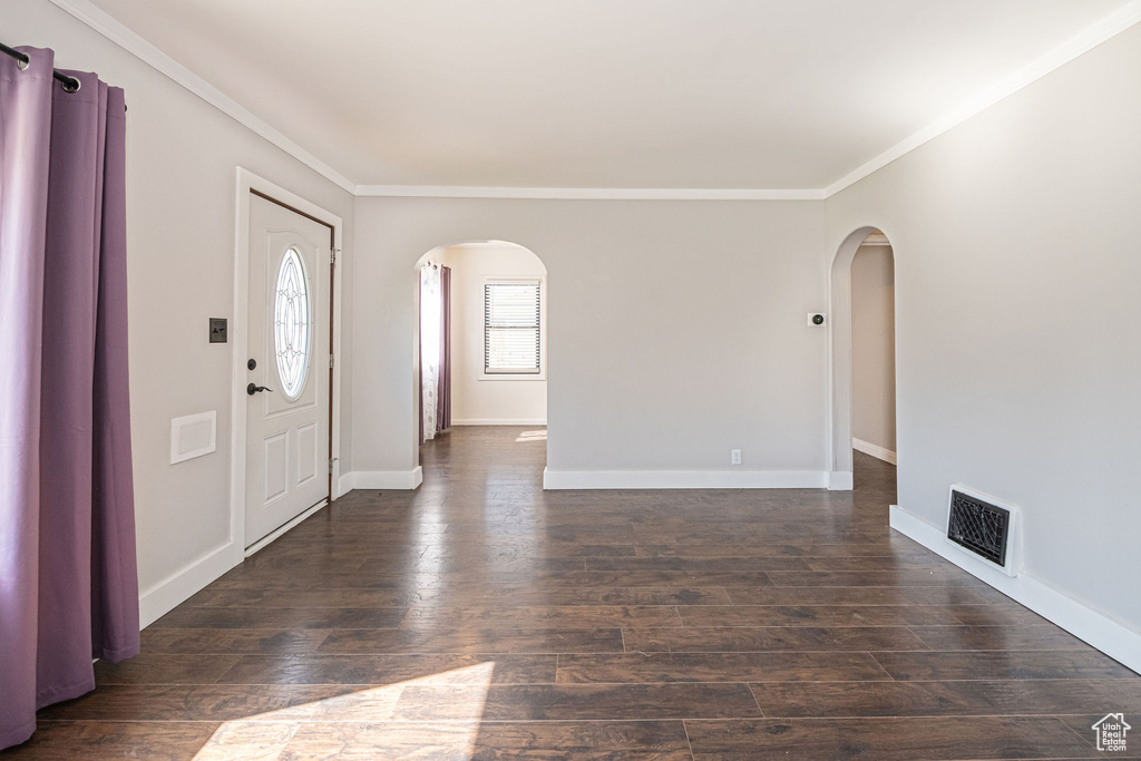 Foyer entrance featuring arched walkways, ornamental molding, dark wood-style flooring, and baseboards