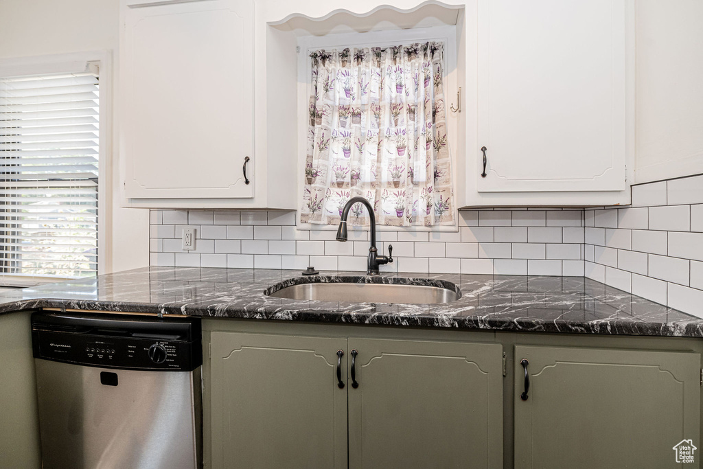 Kitchen featuring stainless steel dishwasher, a sink, decorative backsplash, and white cabinets