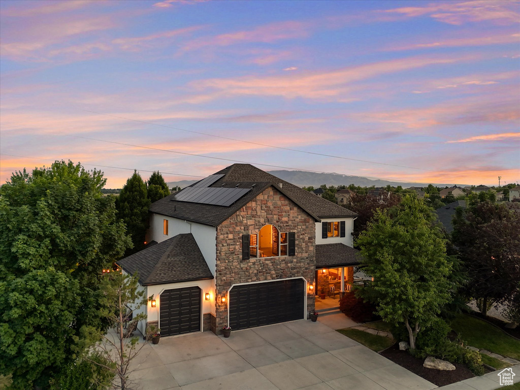 View of front of house featuring stone siding, driveway, roof mounted solar panels, and stucco siding