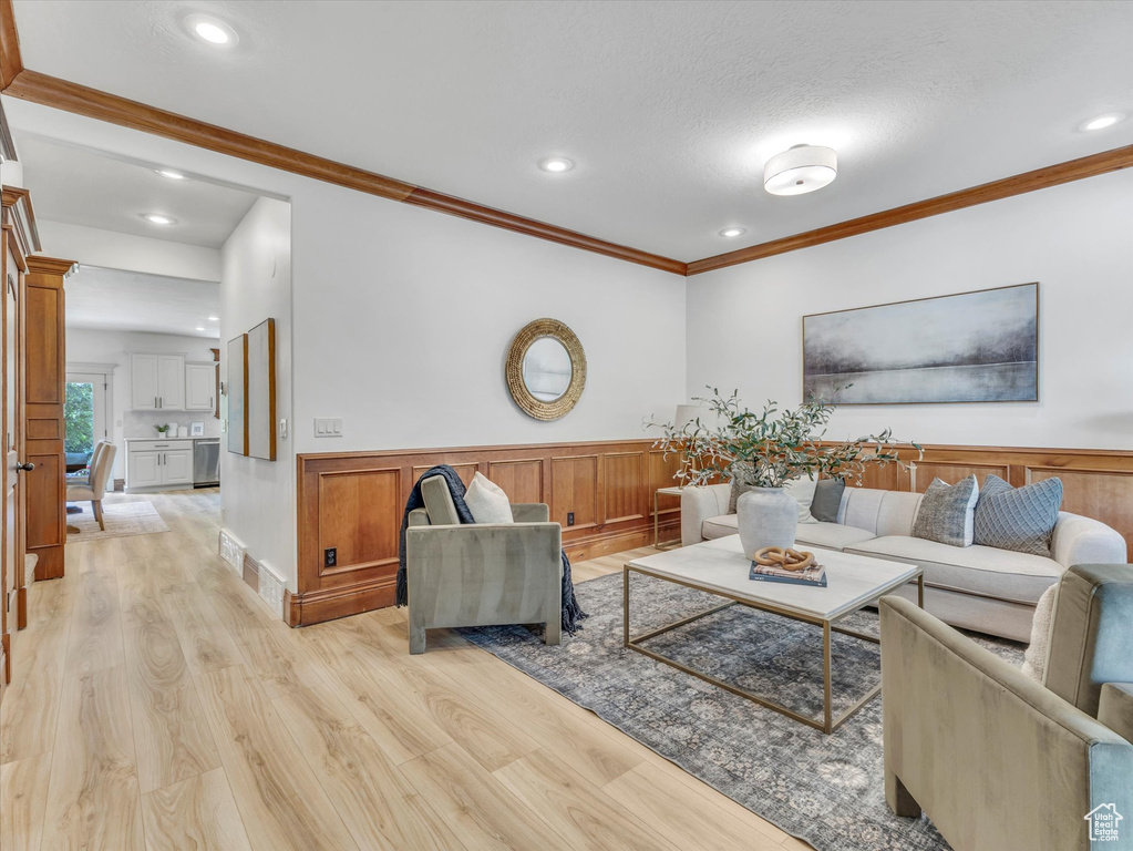Living area with light wood finished floors, a wainscoted wall, ornamental molding, and recessed lighting