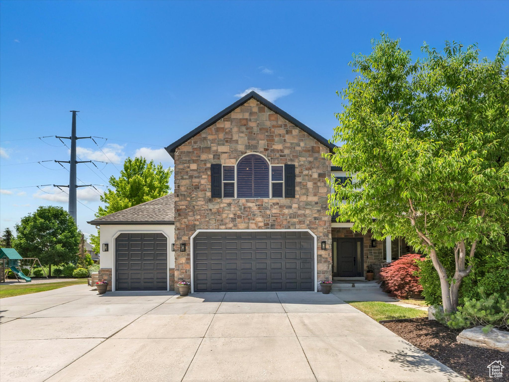 View of front of property with concrete driveway, stone siding, and a garage