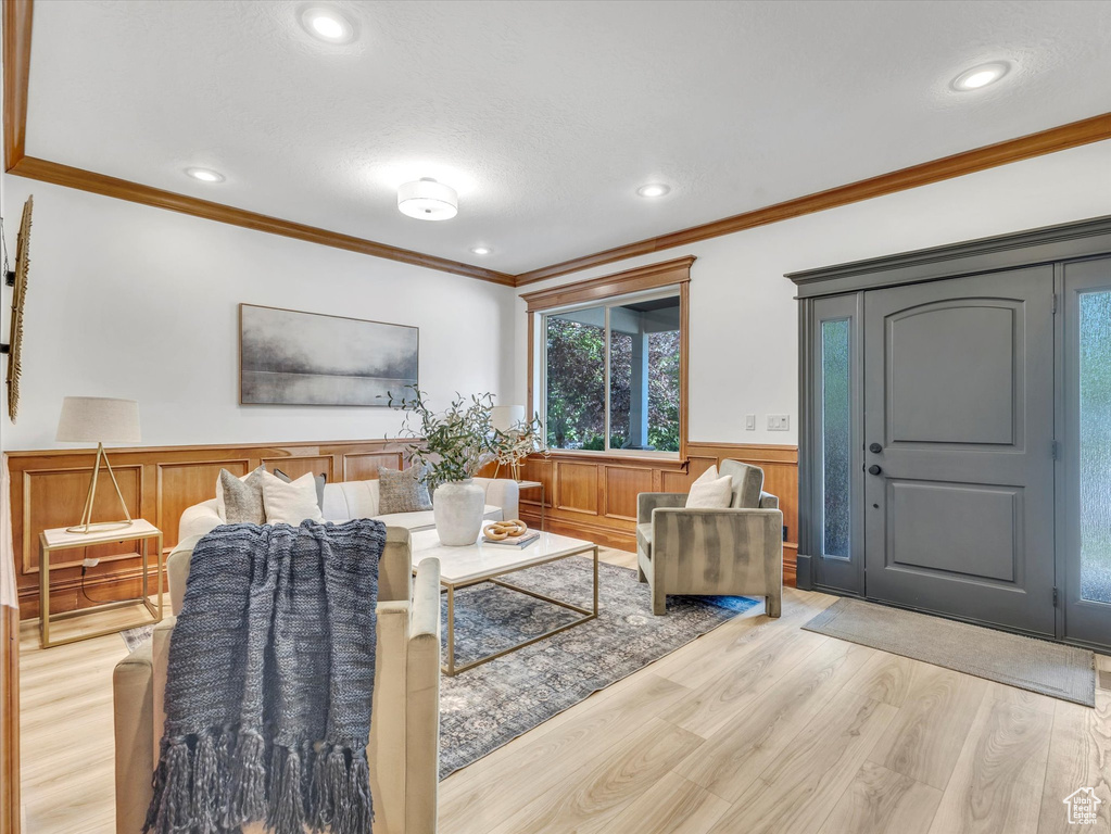 Living room with a wainscoted wall, ornamental molding, light wood-style floors, and recessed lighting