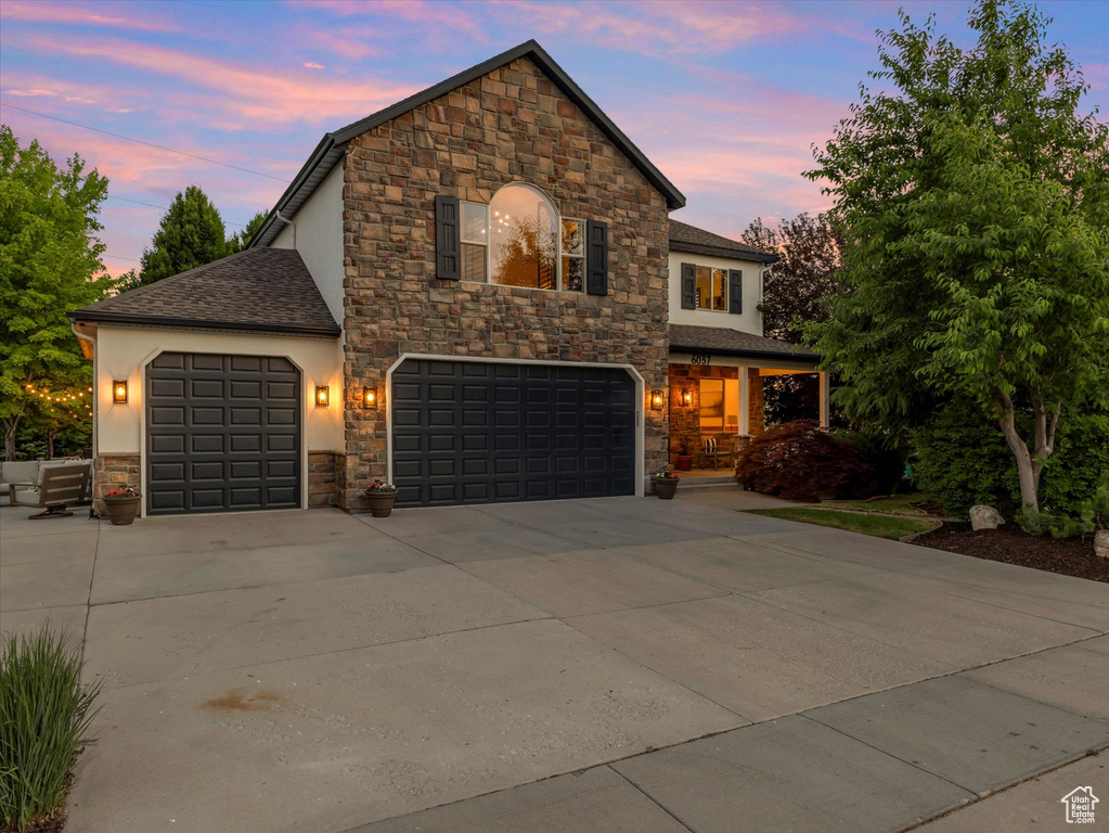 View of front of house with stone siding, driveway, roof with shingles, and stucco siding
