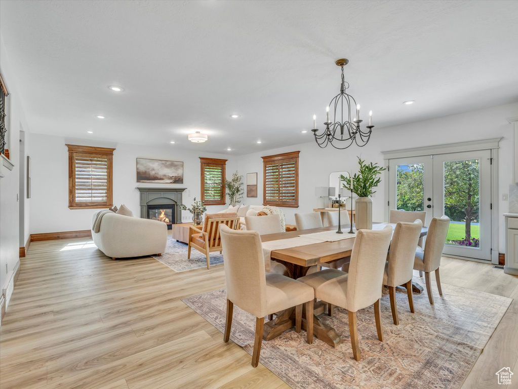 Dining room featuring recessed lighting, light wood-style floors, a glass covered fireplace, french doors, and a chandelier